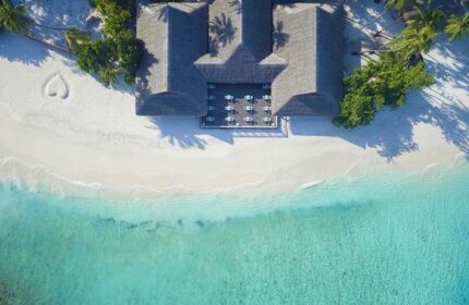 Aerial view of Malahini Kuda Bandos Resort, a gay-friendly hotel. Turquoise water meets white sand beach with a heart drawn in it.