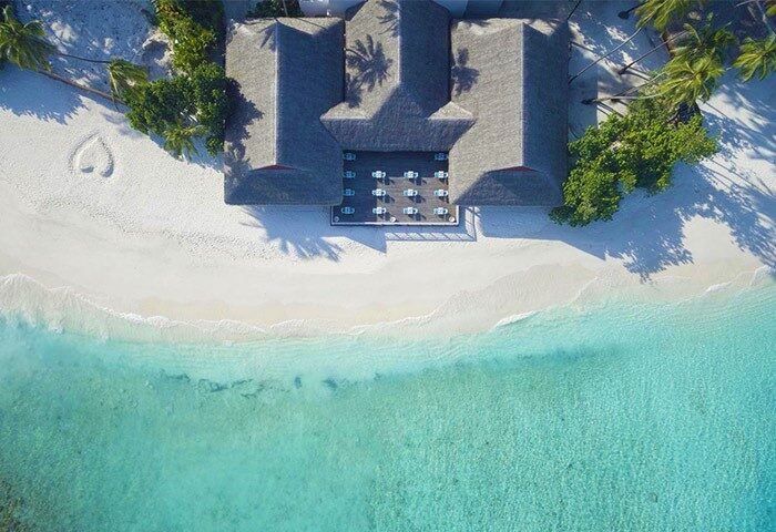 Aerial view of Malahini Kuda Bandos Resort, a gay-friendly hotel. Turquoise water meets white sand beach with a heart drawn in it.