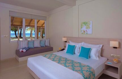 Malahini Kuda Bandos Resort gay-friendly hotel room. Bed with turquoise accents, window seat with ocean view. Relaxing Maldives travel.