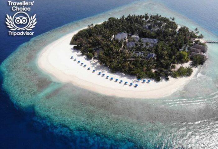 Aerial view of Malahini Kuda Bandos Resort, a gay-friendly hotel. White sand beach, blue umbrellas, and turquoise water surround the island.