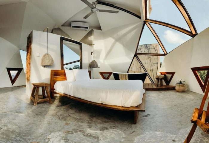 Mamasan Treehouses & Cabins gay-friendly hotel interior. Unique dome-shaped room with bed, bathtub, and triangular windows. Modern, minimalist design.