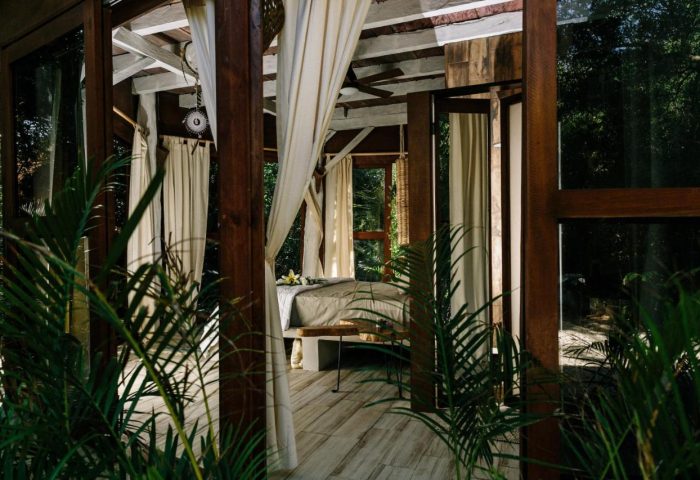 Mamasan Treehouses & Cabins: Interior of a gay-friendly hotel treehouse. Wooden structure with curtains, bed, and lush green plants. Relaxing vibe.