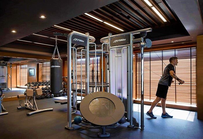 Gay-Friendly Mandarin Oriental Hong Kong gym with punching bag, weights, and man using cable machine. Luxury hotel fitness for gay travelers.