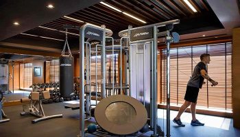 Gay-Friendly Mandarin Oriental Hong Kong gym with punching bag, weights, and man using cable machine. Luxury hotel fitness for gay travelers.