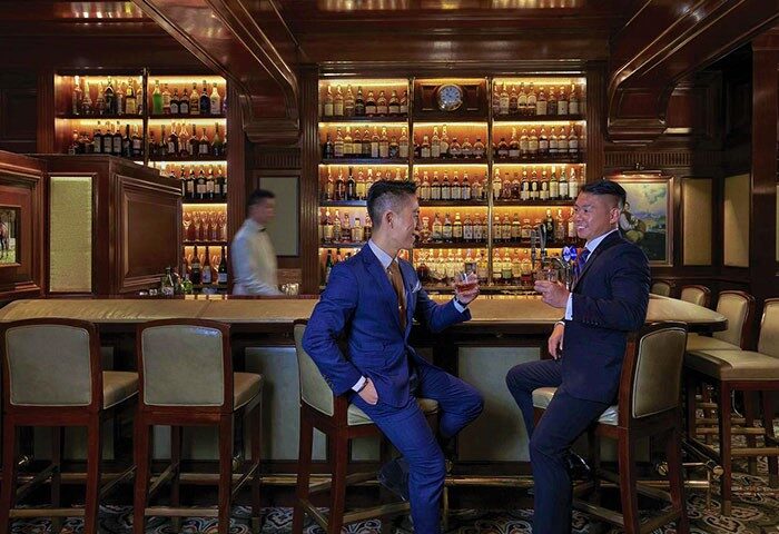 Gay-friendly Mandarin Oriental Hong Kong: Two men in suits enjoy drinks at the hotel bar. Upscale travel for gay men.