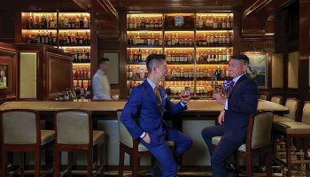 Gay-friendly Mandarin Oriental Hong Kong: Two men in suits enjoy drinks at the hotel bar. Upscale travel for gay men.
