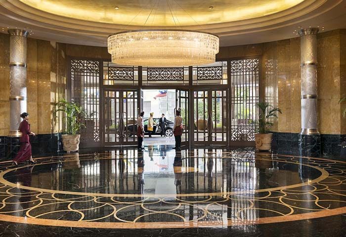 Lobby view at the gay-friendly Mandarin Oriental Kuala Lumpur hotel. Chandelier, marble floor, and staff at the entrance. Luxury travel.