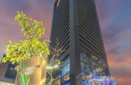 Facade of Manhattan Hotel, a gay-friendly hotel in Manhattan. The building is tall and modern, with a sign pointing towards the entrance.