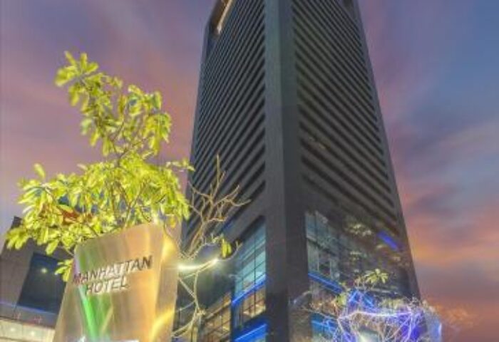 Facade of Manhattan Hotel, a gay-friendly hotel in Manhattan. The building is tall and modern, with a sign pointing towards the entrance.