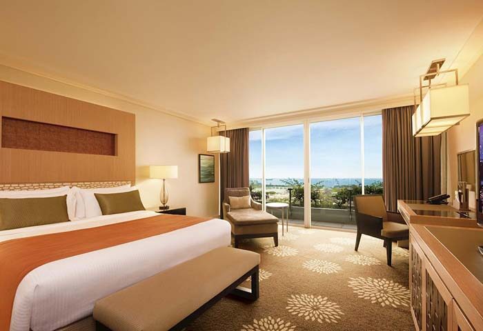 Gay-friendly hotel Marina Bay Sands room. Luxurious suite with ocean view, king bed, chaise lounge, and balcony. Upscale Singapore travel.