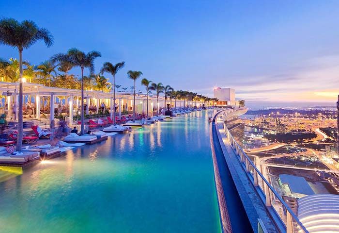 Marina Bay Sands gay-friendly hotel infinity pool at twilight. Palm trees, lounge chairs, and city views. Ideal for gay men's travel.