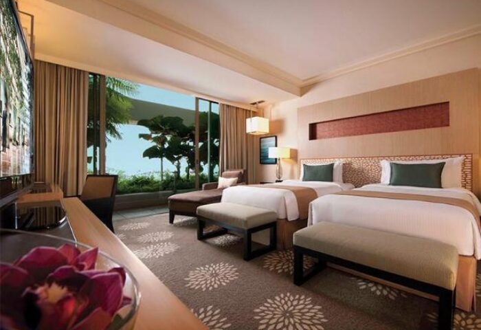 Gay-friendly hotel Marina Bay Sands room. Twin beds, chaise lounge, and balcony with trees. Luxury gay travel in Singapore.