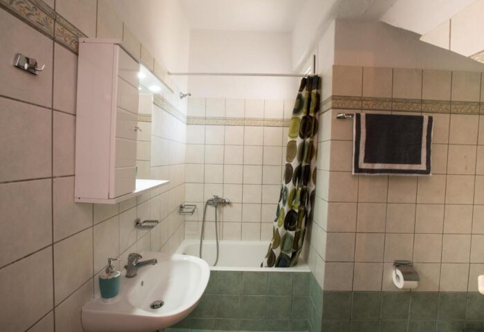 Marina Blue Ornos gay-friendly hotel bathroom. Sink, tub with shower curtain, and tiled walls. Gay travel accommodation in Mykonos.