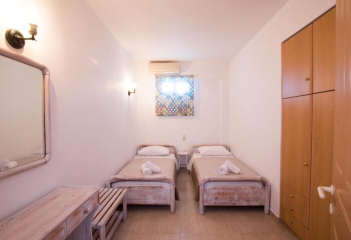 Marina Blue Ornos gay-friendly hotel room. Two twin beds with towels, wardrobe, mirror, desk, and colorful window art. Clean, bright interior.