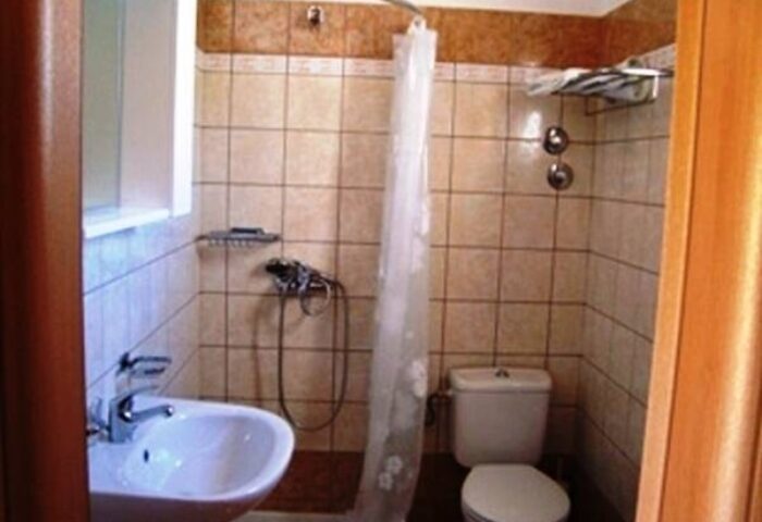 Bathroom at Marina Blue, a gay-friendly hotel in Ornos. Features a sink, toilet, shower with curtain, and tiled walls. For gay travel advice.