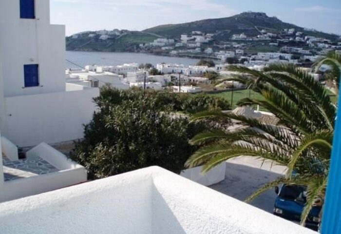View from Marina Blue, a gay-friendly hotel in Ornos, Mykonos. White buildings dot the landscape near the sea, with palm trees in the foreground.