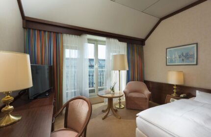 Maritim Hotel Koeln room. Gay-friendly hotel room with bed, desk, chair, and balcony. Comfortable stay in Cologne, Germany.