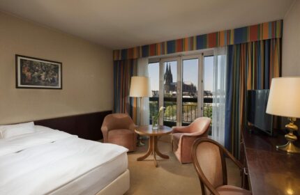 Maritim Hotel Koeln room with Cologne Cathedral view. Gay-friendly hotel room interior with bed, chairs, desk, and balcony. Cologne travel.