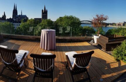 Rooftop terrace at Maritim Hotel Koeln, a gay-friendly hotel. Deck chairs, table, and Cologne Cathedral view. Relaxing space for gay travelers.