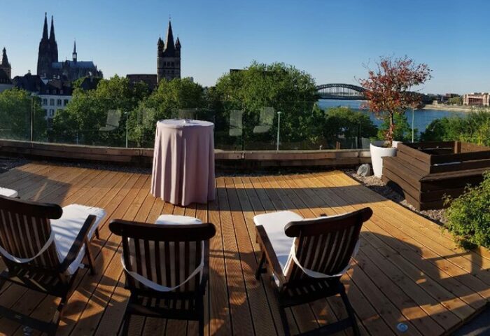 Rooftop terrace at Maritim Hotel Koeln, a gay-friendly hotel. Deck chairs, table, and Cologne Cathedral view. Relaxing space for gay travelers.
