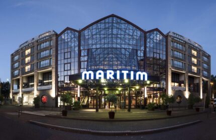 Maritim Hotel Koeln exterior at dusk. Gay-friendly hotel with glass facade. A top choice for gay men visiting Cologne, Germany.
