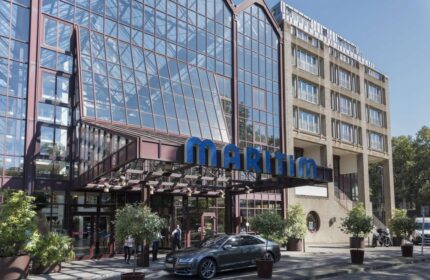 Maritim Hotel Koeln entrance. Gay-friendly hotel with glass facade. The Maritim sign is prominently displayed. Car parked in front.