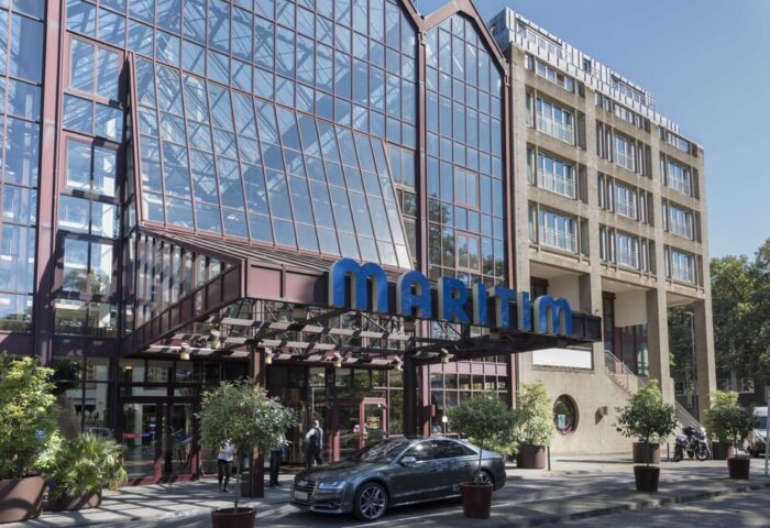 Maritim Hotel Koeln entrance. Gay-friendly hotel with glass facade. The Maritim sign is prominently displayed. Car parked in front.