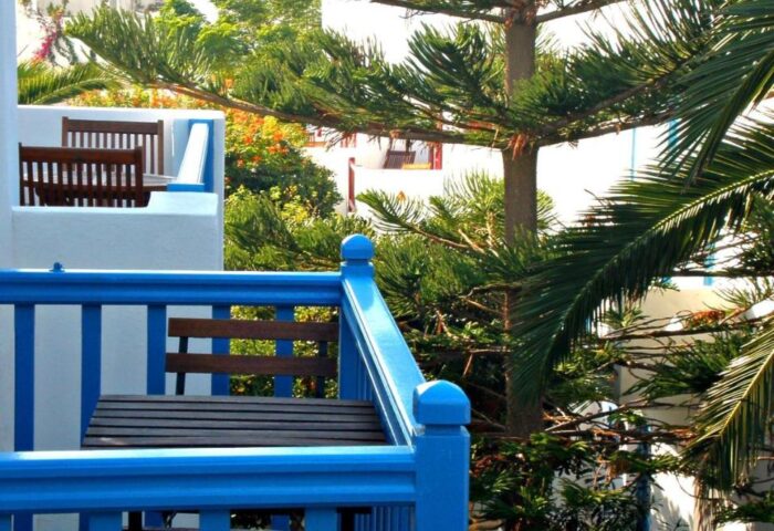 Gay-friendly Matina Hotel balcony view. Blue railings, table and chairs. Lush greenery. Idyllic gay travel destination.