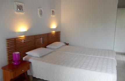 Gay-friendly Matina Hotel bedroom. Two twin beds with a wooden headboard and white bedding. Nightstand with a purple lamp.
