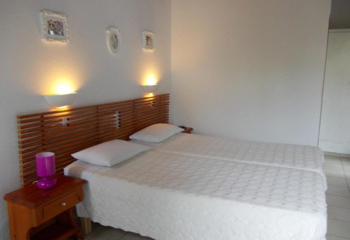 Gay-friendly Matina Hotel bedroom. Two twin beds with a wooden headboard and white bedding. Nightstand with a purple lamp.