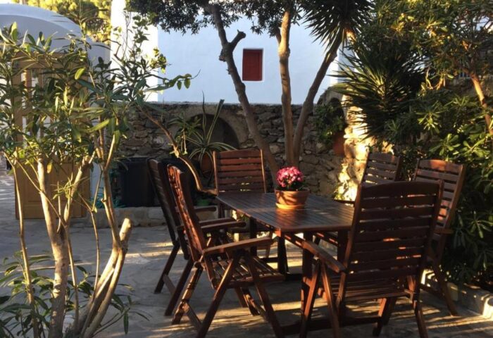 Matina Hotel outdoor dining area. Table and chairs on stone patio surrounded by trees. Gay-friendly hotel for gay men travel advice.