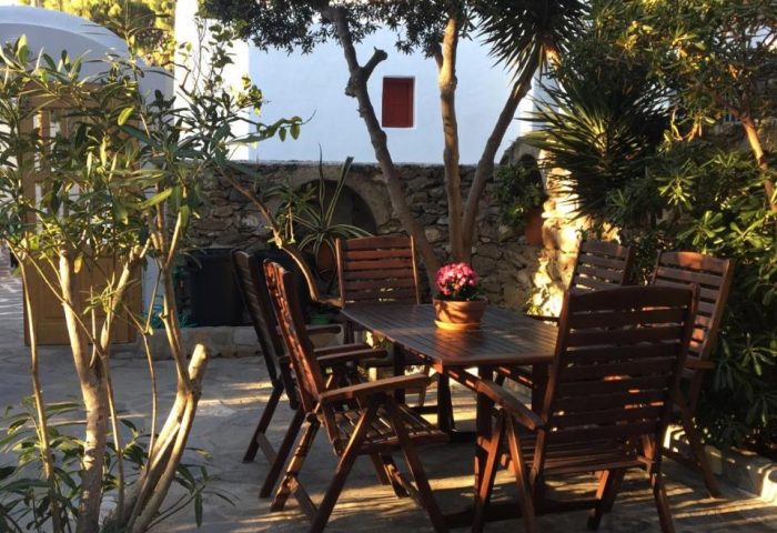 Matina Hotel outdoor dining area. Table and chairs on stone patio surrounded by trees. Gay-friendly hotel for gay men travel advice.
