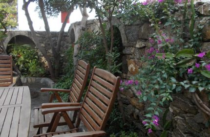 Gay-friendly Matina Hotel seating area. Wooden chairs, stone wall with arches, and bougainvillea. Ideal for gay men's travel and relaxation.