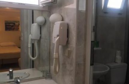Bathroom interior at Matina Hotel, a gay-friendly hotel. Sink, mirror, hair dryer, toilet, and window visible. Gay travel accommodations.