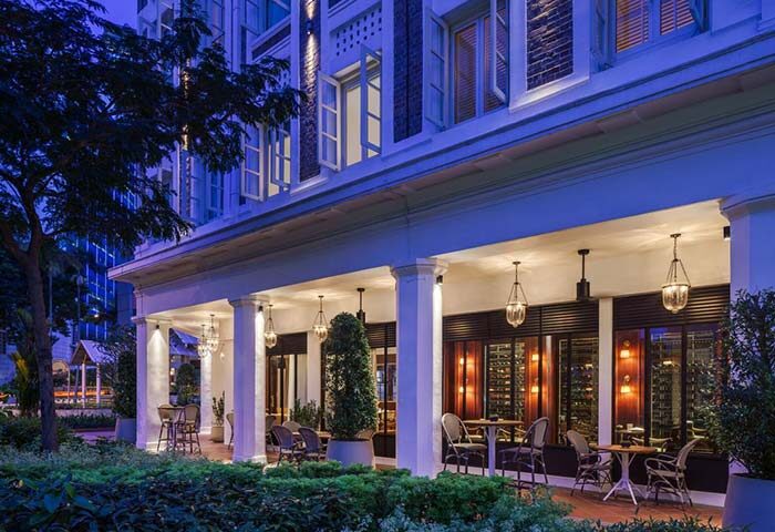 Maxwell Reserve, a gay-friendly hotel. Outdoor patio with tables and chairs under a covered walkway. Elegant building at night.