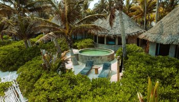 Maya Tulum By G Hotels: Gay-friendly hotel view with thatched-roof cabanas, pool, lounge chairs, and lush greenery. Tropical gay travel.