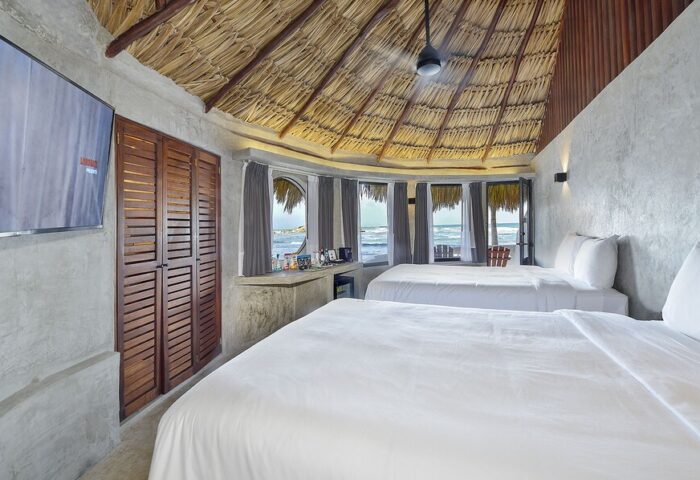 Gay-friendly Maya Tulum By G Hotels room. Two beds, thatched roof, ocean view. Perfect for gay travel and relaxation in Tulum.