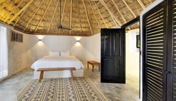 Bedroom at Maya Tulum By G Hotels, a gay-friendly hotel. Thatched roof, white walls, king bed, patterned rug. Stylish gay travel lodging.