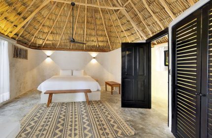Bedroom at Maya Tulum By G Hotels, a gay-friendly hotel. Thatched roof, white walls, king bed, patterned rug. Stylish gay travel lodging.