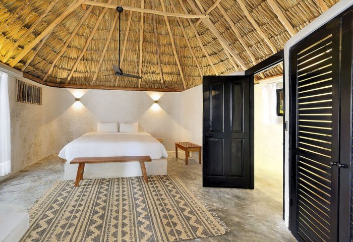 Bedroom at Maya Tulum By G Hotels, a gay-friendly hotel. Thatched roof, white walls, king bed, patterned rug. Stylish gay travel lodging.