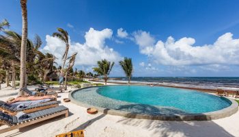 Maya Tulum By G Hotels gay-friendly hotel pool. Beachfront view with palm trees, lounge chairs, and blue skies. Perfect for gay travel.