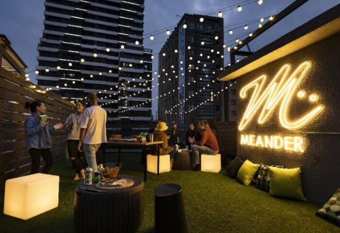 Meander Taipei Hostel Ximending rooftop lounge. Gay-friendly hotel with city views, string lights, and a neon Meander logo. Social gathering.
