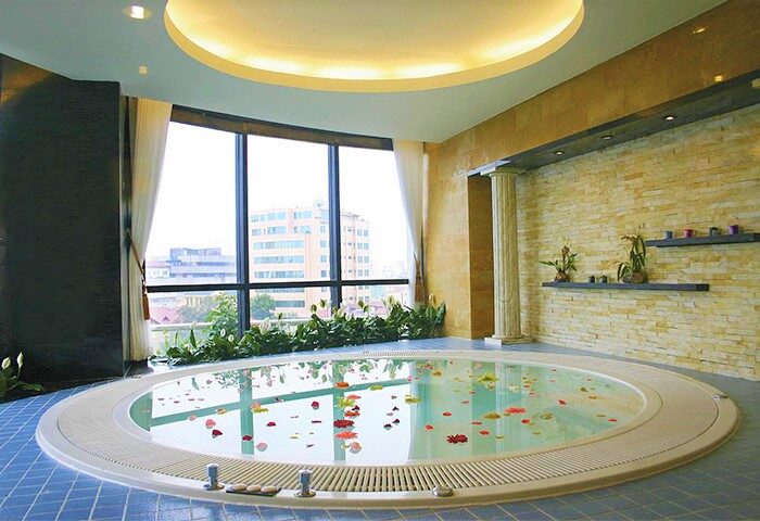 Gay-friendly Melia Hanoi Hotel spa. Round jacuzzi with flower petals, large windows, and city view. Relaxing space for gay travelers.