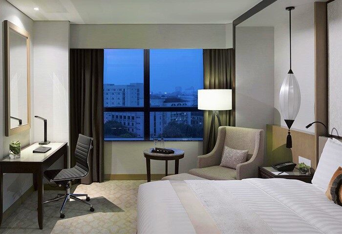 Melia Hanoi Hotel room. Gay-friendly hotel featuring a desk, chair, bed, and city view. Modern interior design at Melia Hanoi Hotel.
