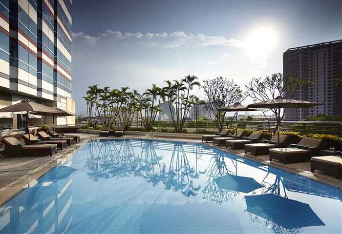 Pool at the gay-friendly Melia Hanoi Hotel. Loungers and umbrellas line the pool deck. City view. Relaxing gay travel.