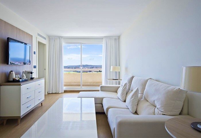 Melia Sitges gay-friendly hotel room. Modern interior with white sofa, TV, and balcony with a view. Luxury gay travel in Sitges, Spain.