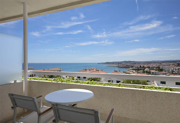 Balcony view at Melia Sitges, a gay-friendly hotel. Table and chairs overlook the Mediterranean Sea and the Sitges skyline. Perfect for gay travel.