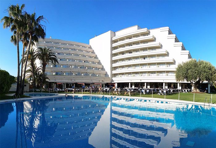 Melia Sitges gay-friendly hotel view. Pool reflects the building's architecture. Palm trees add to the relaxing atmosphere.