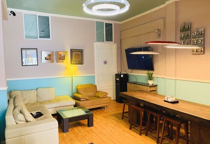 Melrose Hostel Adults Only common area. Gay-friendly hotel with couches, a long table with stools, and modern lighting. Relaxing space.