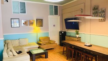 Melrose Hostel Adults Only common area. Gay-friendly hotel with couches, a long table with stools, and modern lighting. Relaxing space.